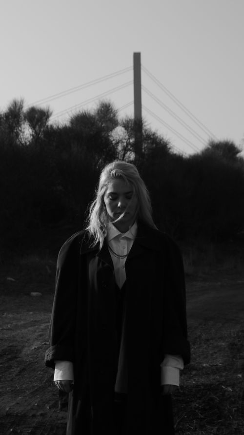 Free Black and white photo of a woman in an oversized coat against an outdoor backdrop. Stock Photo
