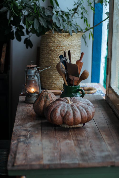 Pumpkins and Kitchen Utensils On Wooden Table Beside A Lantern and Houseplant