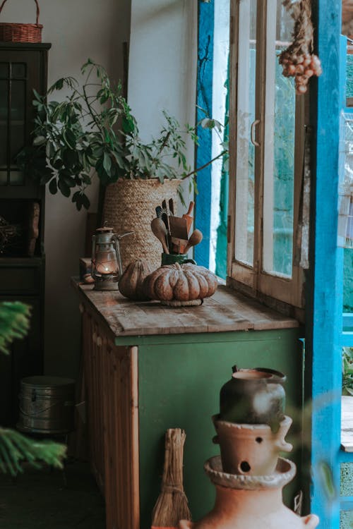 Room interior with various ceramic pots near windowsill with potted green plant and kitchenware near old kerosene lamp in daylight