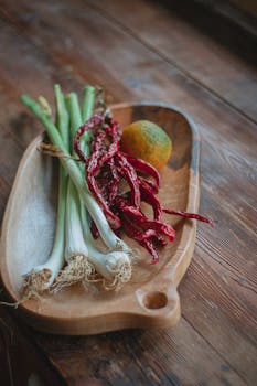 A close-up of fresh vegetables and spices in a wooden dish on a rustic table.