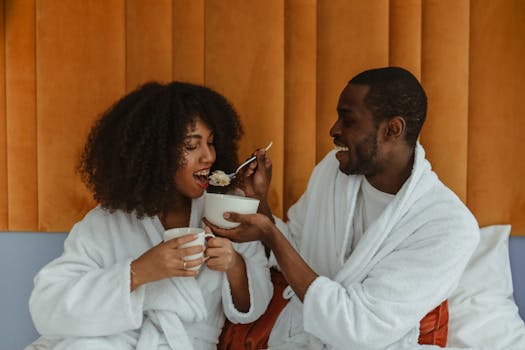 Happy couple in bathrobes enjoying breakfast together with cereal and coffee.
