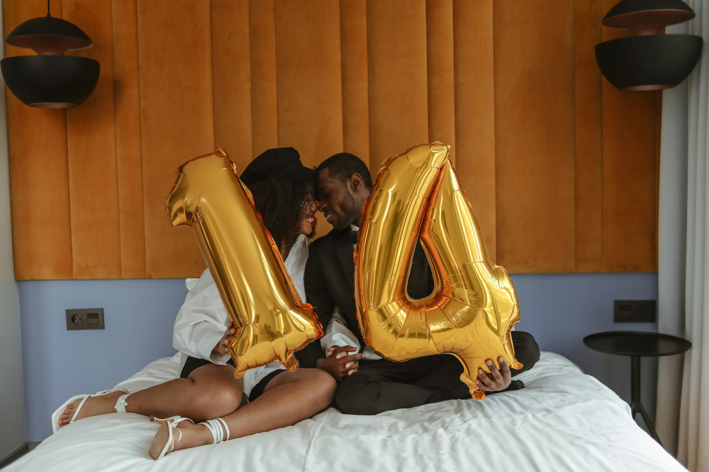 a couple sitting on the bed while holding a number balloon