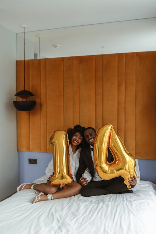 Free Couple Sitting on Bed While Holding Balloons Stock Photo