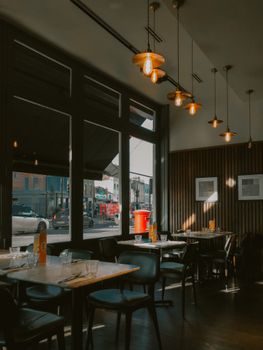 Inviting restaurant interior with empty tables, pendant lights, and street view through large windows.