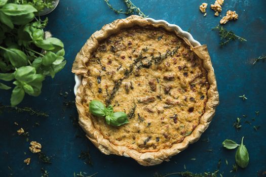 Delicious homemade quiche with fresh herbs on rustic blue surface, perfect for culinary presentations.