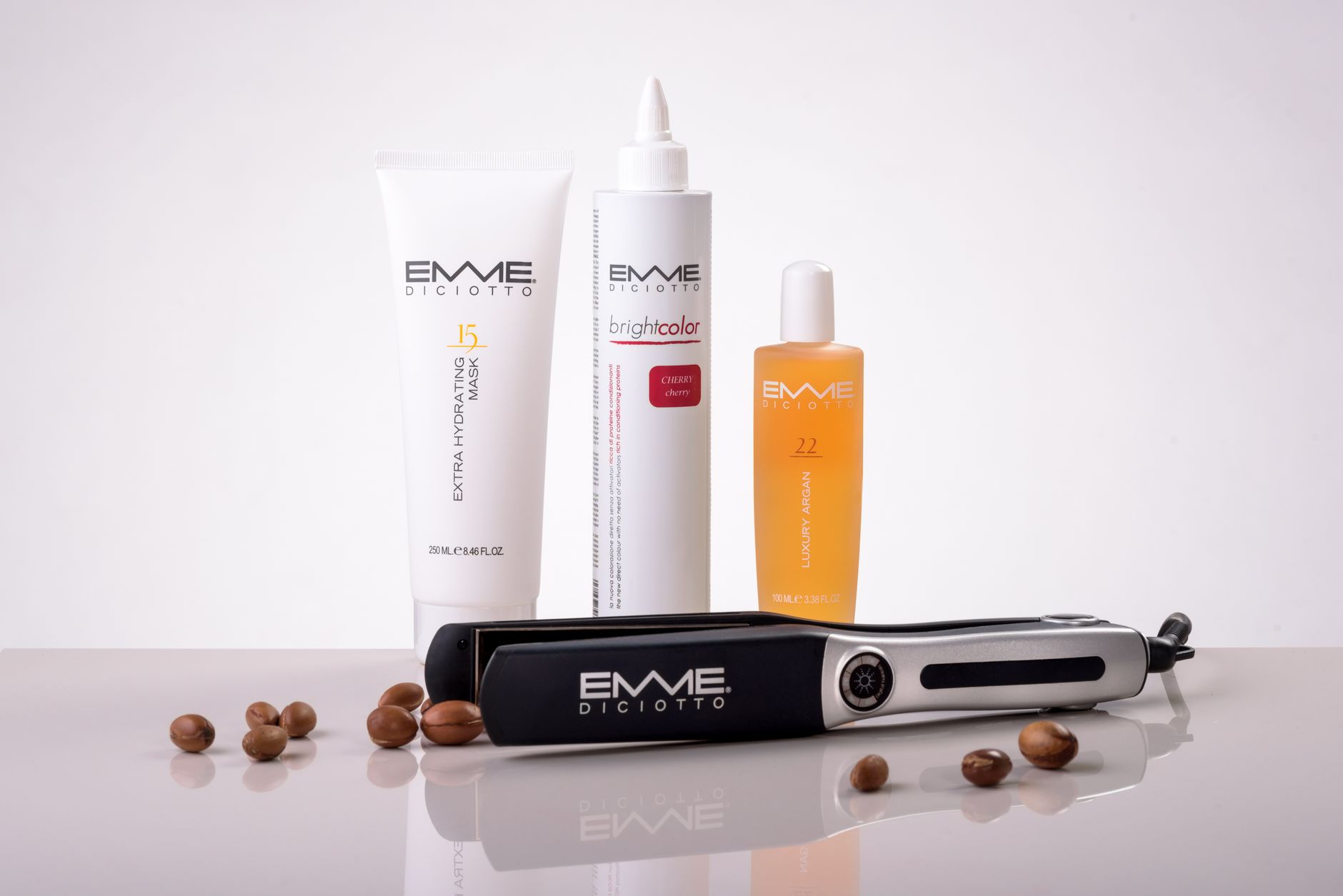 Hair care products and a flat iron by EMME Diciotto on a reflective surface for beauty routines.