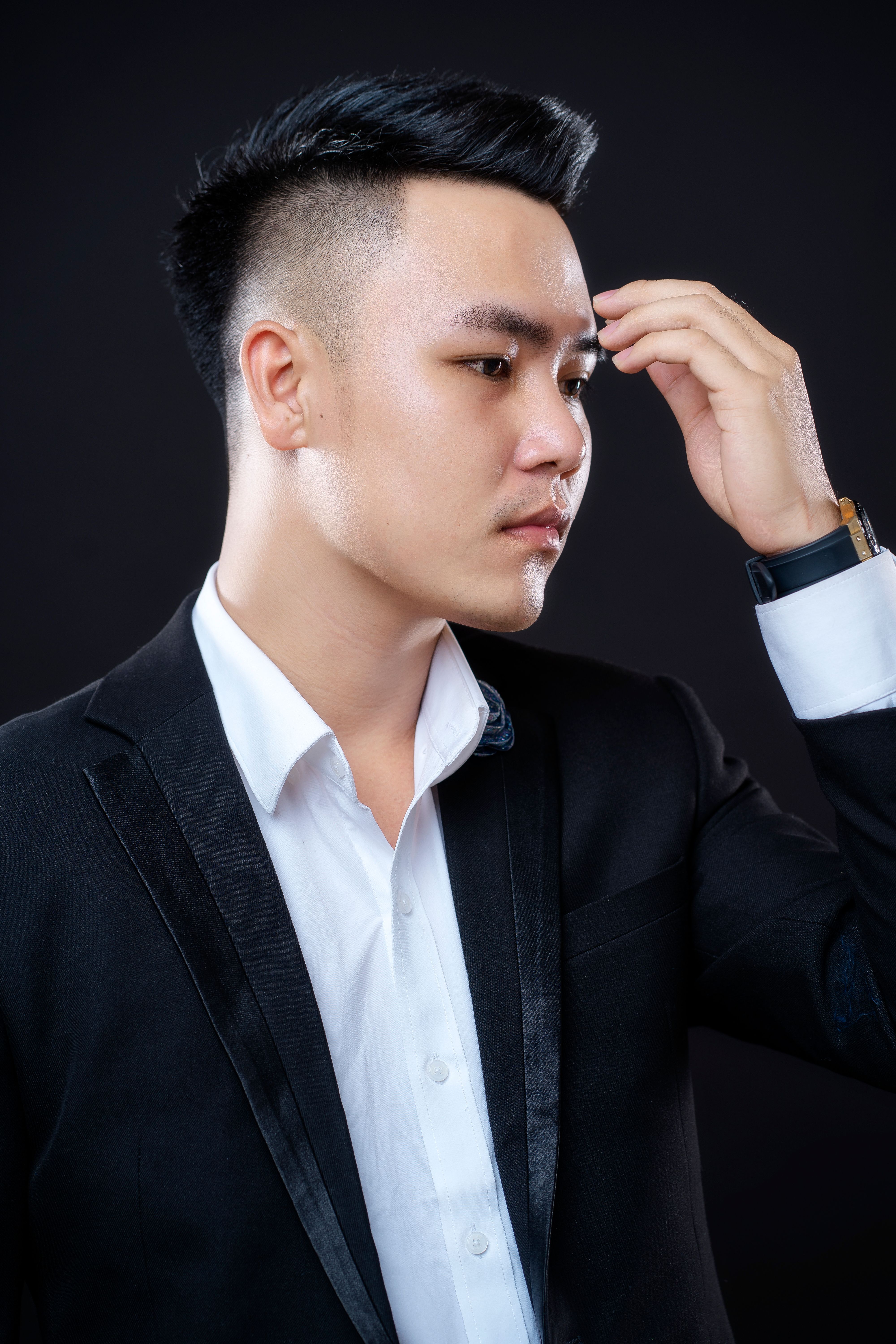 Portrait of an Asian man in a suit jacket, hand near face, studio setting.