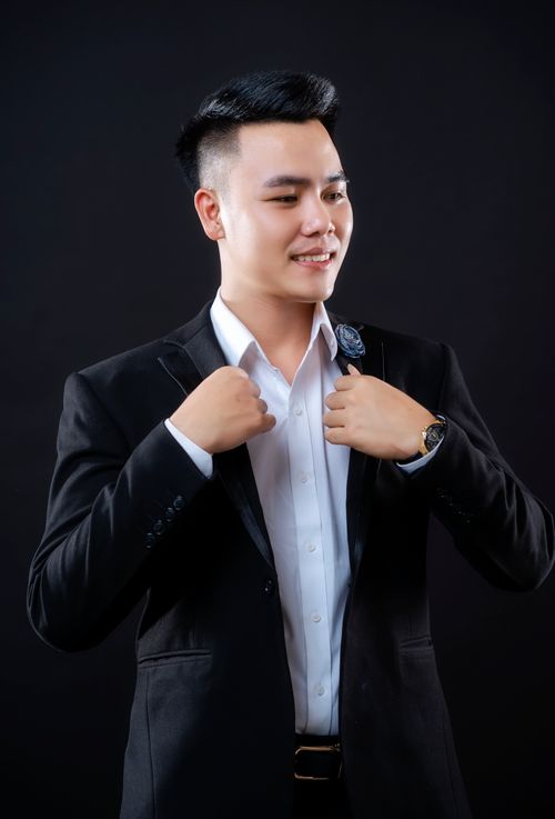 Free Asian man in a suit adjusting collar, smiling in studio setting. Stock Photo