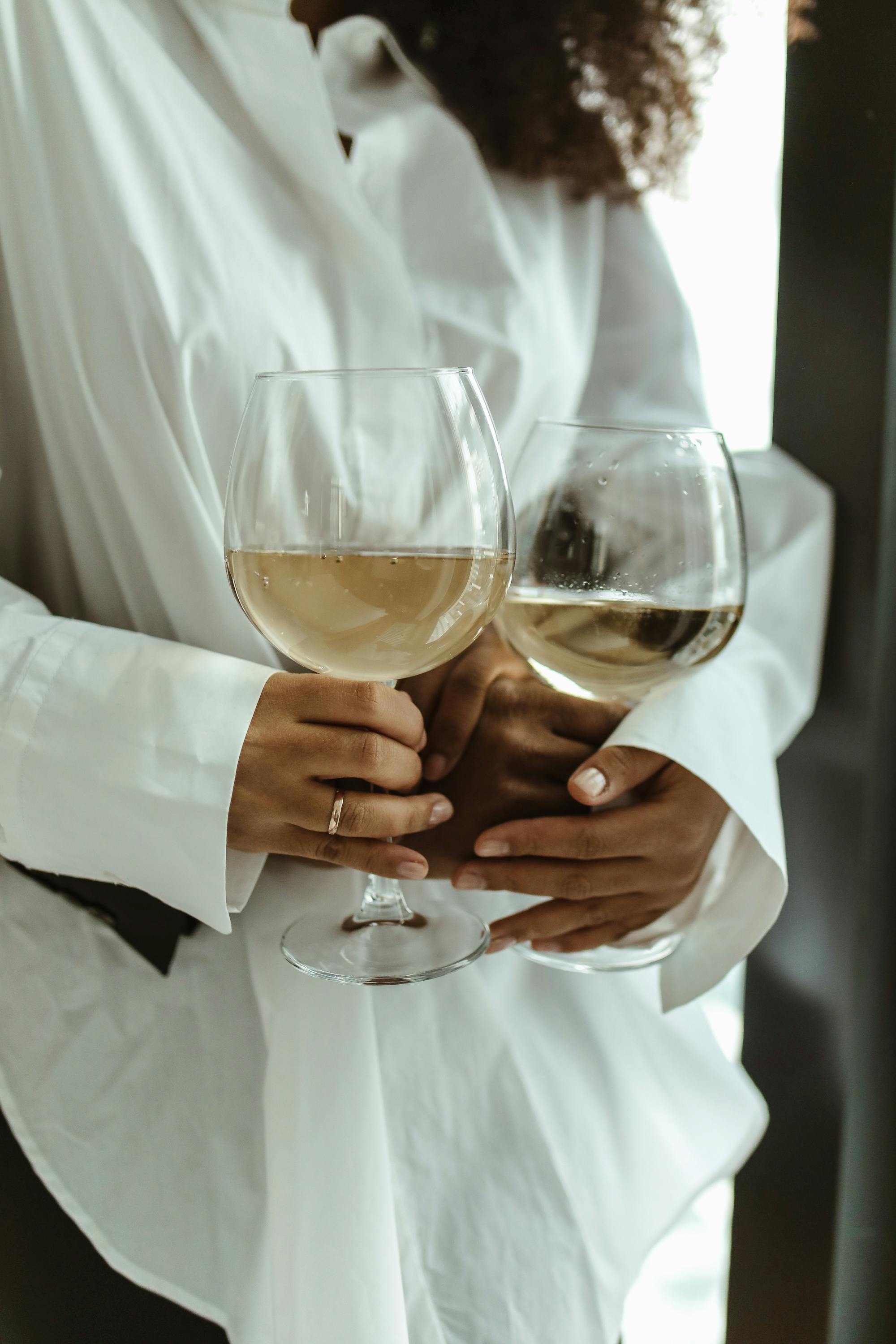 Close-up of an elegant couple holding glasses of white wine in an intimate setting.