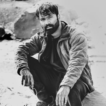 Black and white portrait of a bearded man sitting outdoors in India.