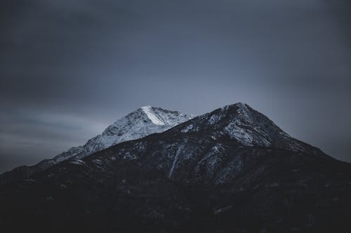 Amazing scenery of rocky mountains with snowy peaks against cloudy dramatic sky in winter evening
