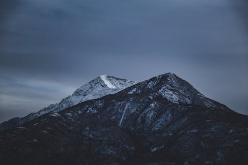 Breathtaking landscape of massive rocky mountains with snowy snowy peaks against against overcast gray sky in winter