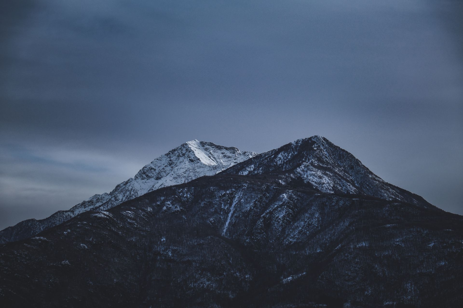 Breathtaking landscape of massive rocky mountains with snowy snowy peaks against against overcast gray sky in winter