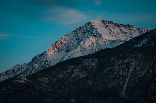 Free Majestic landscape of snowy mountains covered with with lush coniferous trees against cloudy blue sky at sunset Stock Photo
