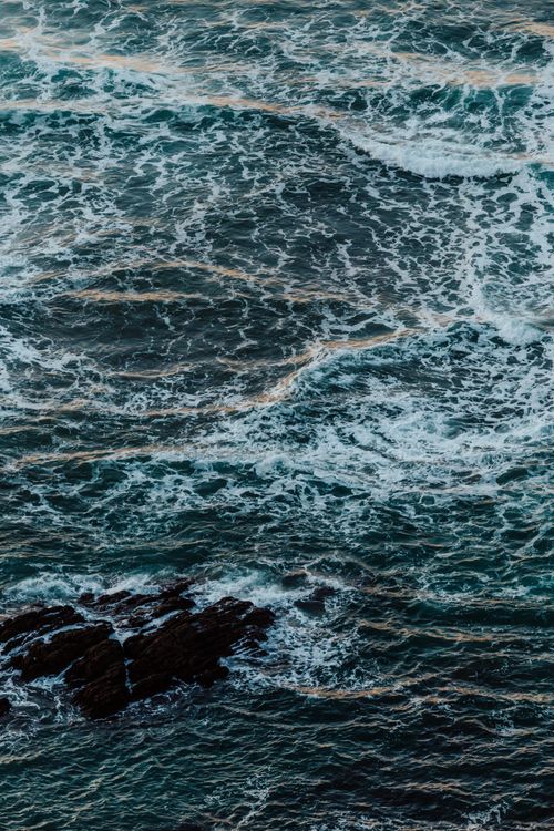 Free Stunning aerial shot of ocean waves forming beautiful patterns around coastal rocks. Stock Photo