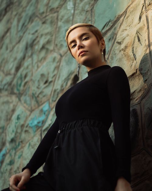 Free From below of young confident lady in trendy black outfit standing near uneven shabby surface and looking at camera thoughtfully Stock Photo