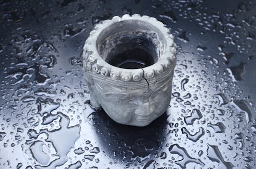 Old Buddha head shaped clay pot on dark wet table