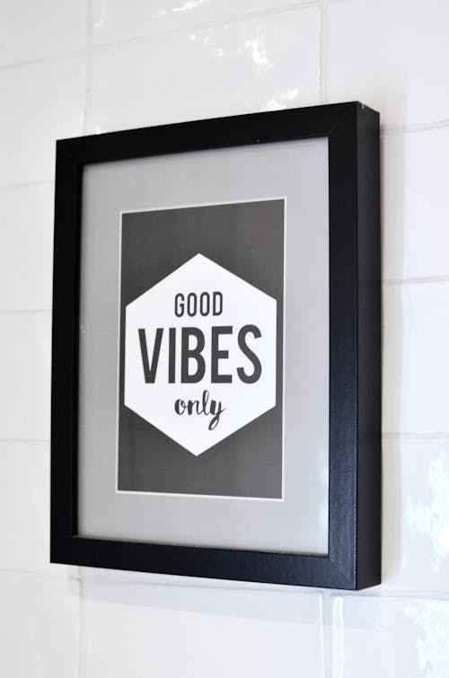Free Picture in wooden frame with Good Vibes Only inscription hanging on white tiled wall Stock Photo
