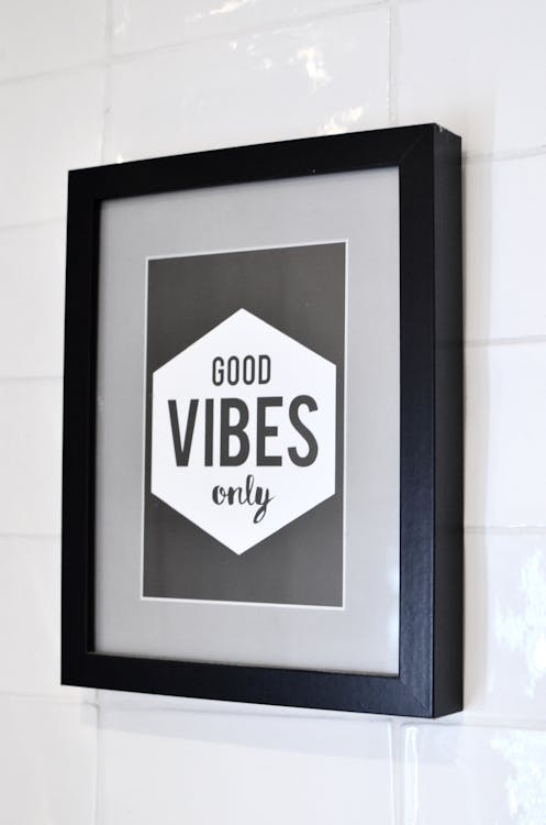 Free Picture in wooden frame with Good Vibes Only inscription hanging on white tiled wall Stock Photo