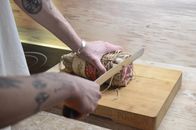 Crop man cutting meat on wooden board at home