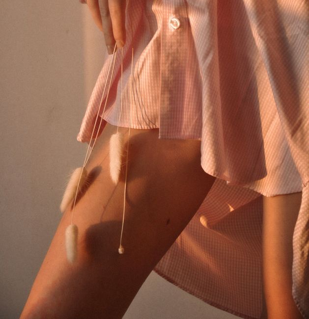 Unrecognizable crop female wearing shirt gently touching legs with dry branches standing in sunshine