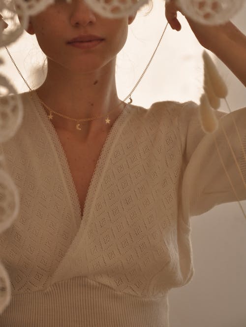 Crop female reflecting in mirror while putting on golden necklace with decorative pendants