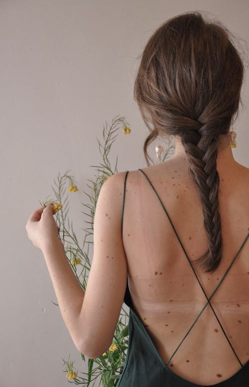 Free Back view of unrecognizable female with pigtail on bare skin near blooming plant Stock Photo