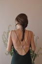 Back view of unrecognizable female in black dress with bare back marks standing near blossoming flowers