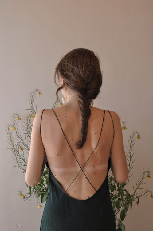 Back view of unrecognizable female in black dress with bare back marks standing near blossoming flowers
