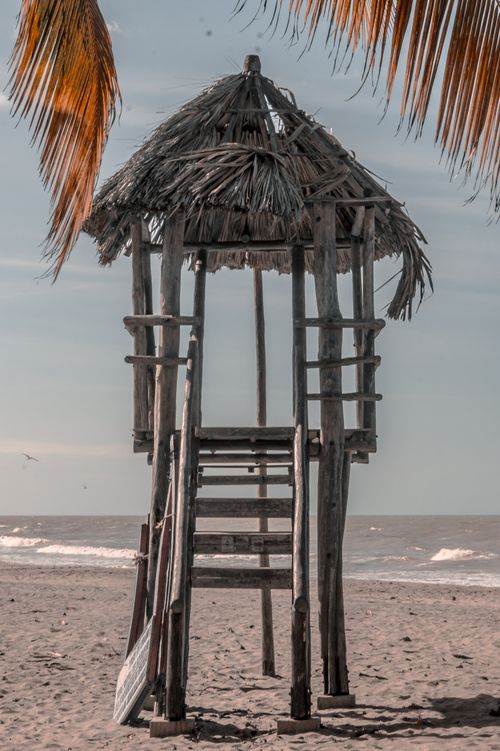 Free A wooden lifeguard tower stands on a serene tropical beach with palm leaves overhead. Stock Photo