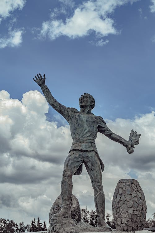 A Statue of a Man Under White Clouds and Blue Sky