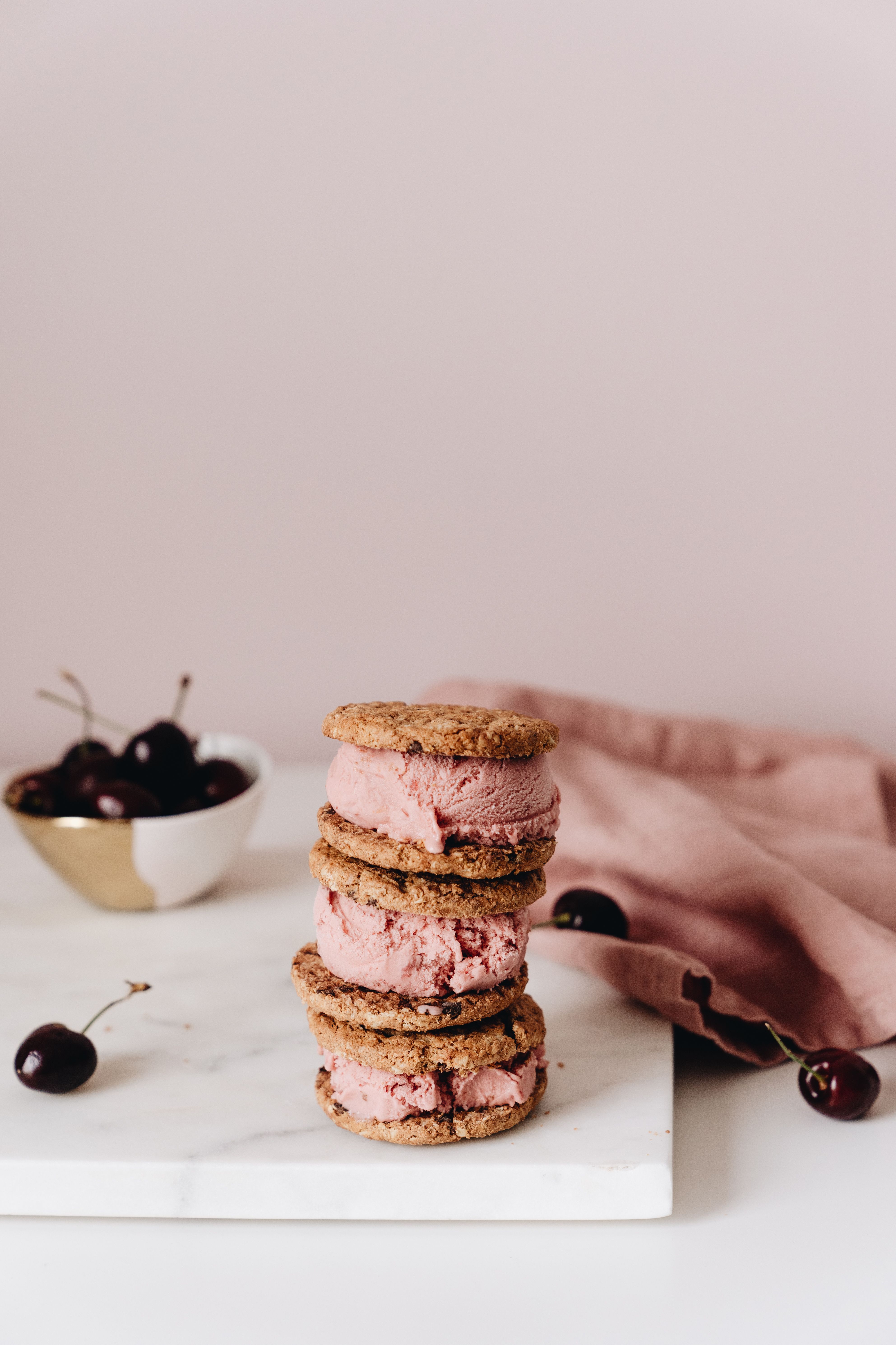 Stack of cherry ice cream cookie sandwiches with cherries on a marble slab, artistic styling.