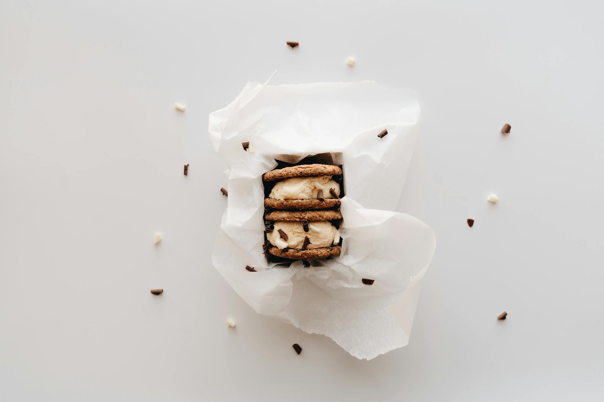 Close-up of a cookie sandwich ice cream wrapped in white paper, surrounded by chocolate sprinkles.