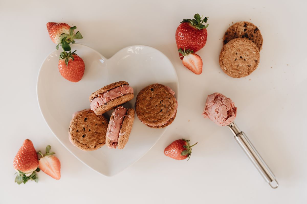 High-angle view of strawberry ice cream cookie sandwiches with fresh strawberries on a heart-shaped plate.