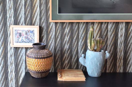 Creative wooden vase with potted cactus plant and notebook placed on table near wall decorated with framed pictures in modern apartment