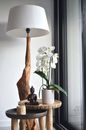 Elegant white potted orchid flowers placed on small wooden table with Buddha statuette and candle near creative lamp in modern apartment