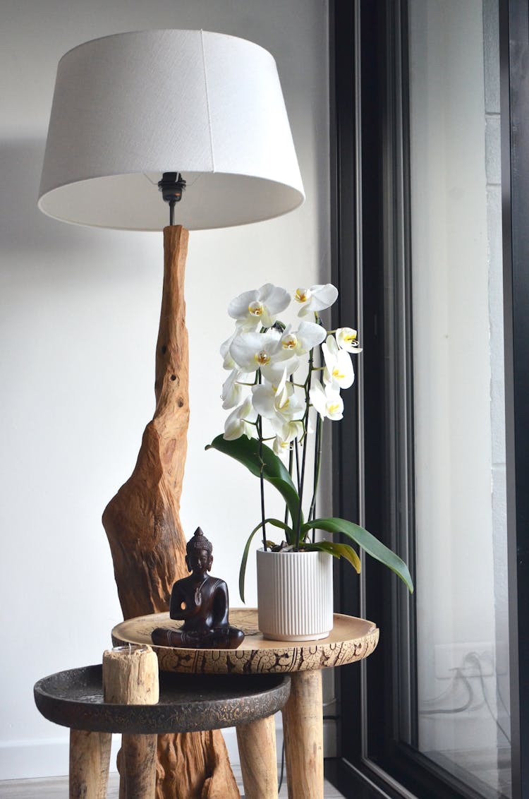 Big Wooden Lamp Placed Near Table With Potted Orchids And Buddha Statuette