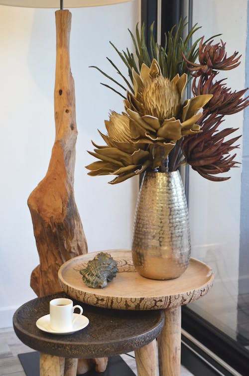 Decorative wooden plants in vase near shell and small ceramic cup of aromatic hot drink at home