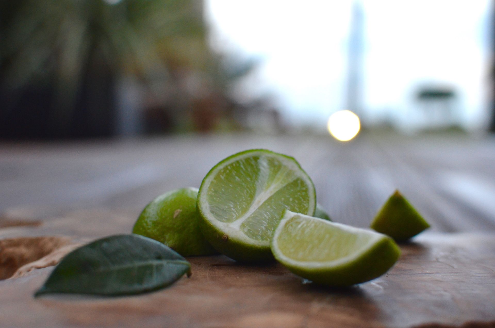 A close-up of sliced lime and a leaf on a rustic surface with a blurred outdoor background.