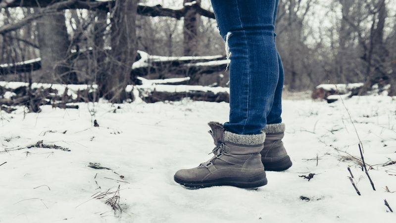 Person in winter boots and jeans, snowy forest path