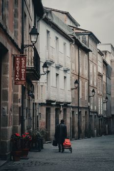 A person walking down a historic street in Orense, Spain, with beautiful architecture and street lamps.
