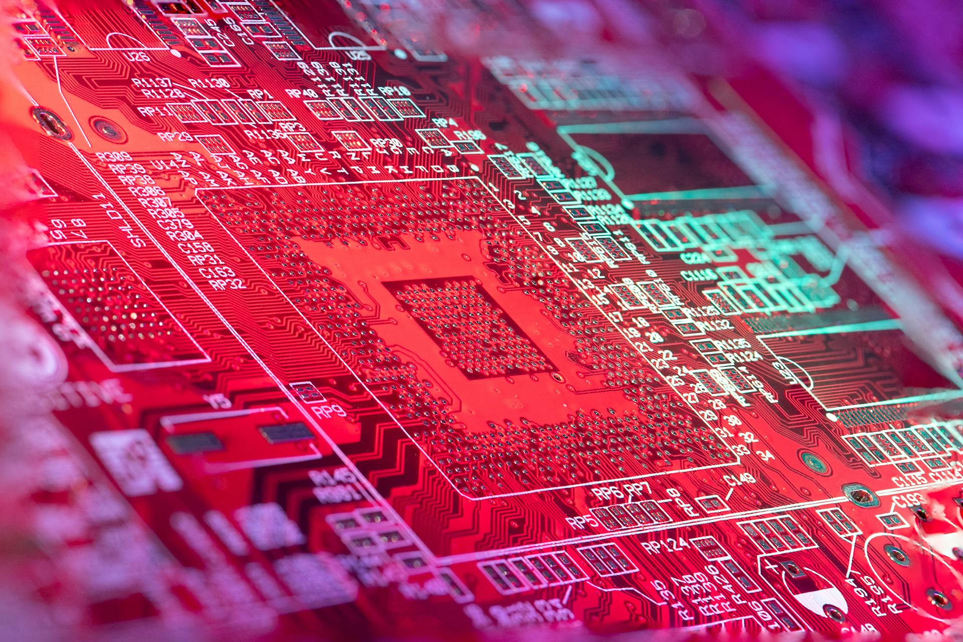 Red printed board of digital device with bright electric circuit with numbers and symbols placed in room on blurred background