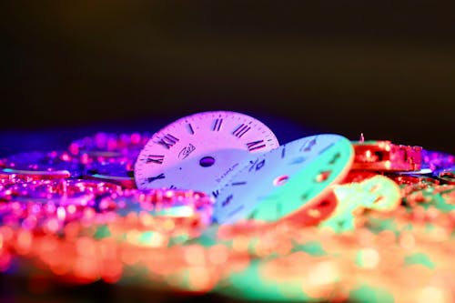 Round clock faces with Roman and Arabic numerals placed among stack of watch movements in dark room on black background