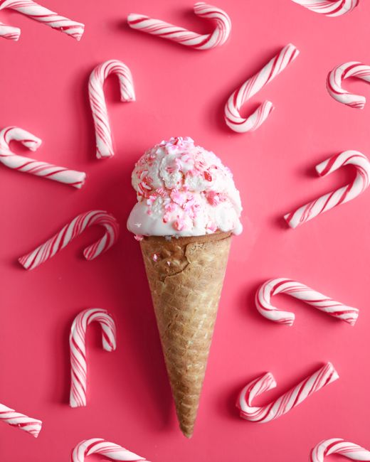 Ice cream cone with candy cane sprinkles on a bright pink surface, ideal for festive and indulgent themes.