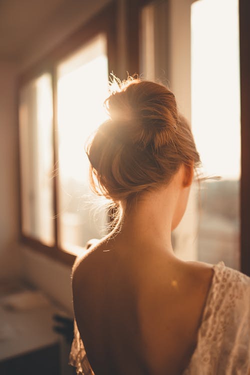 Unrecognizable woman with hair bun at home in sunshine