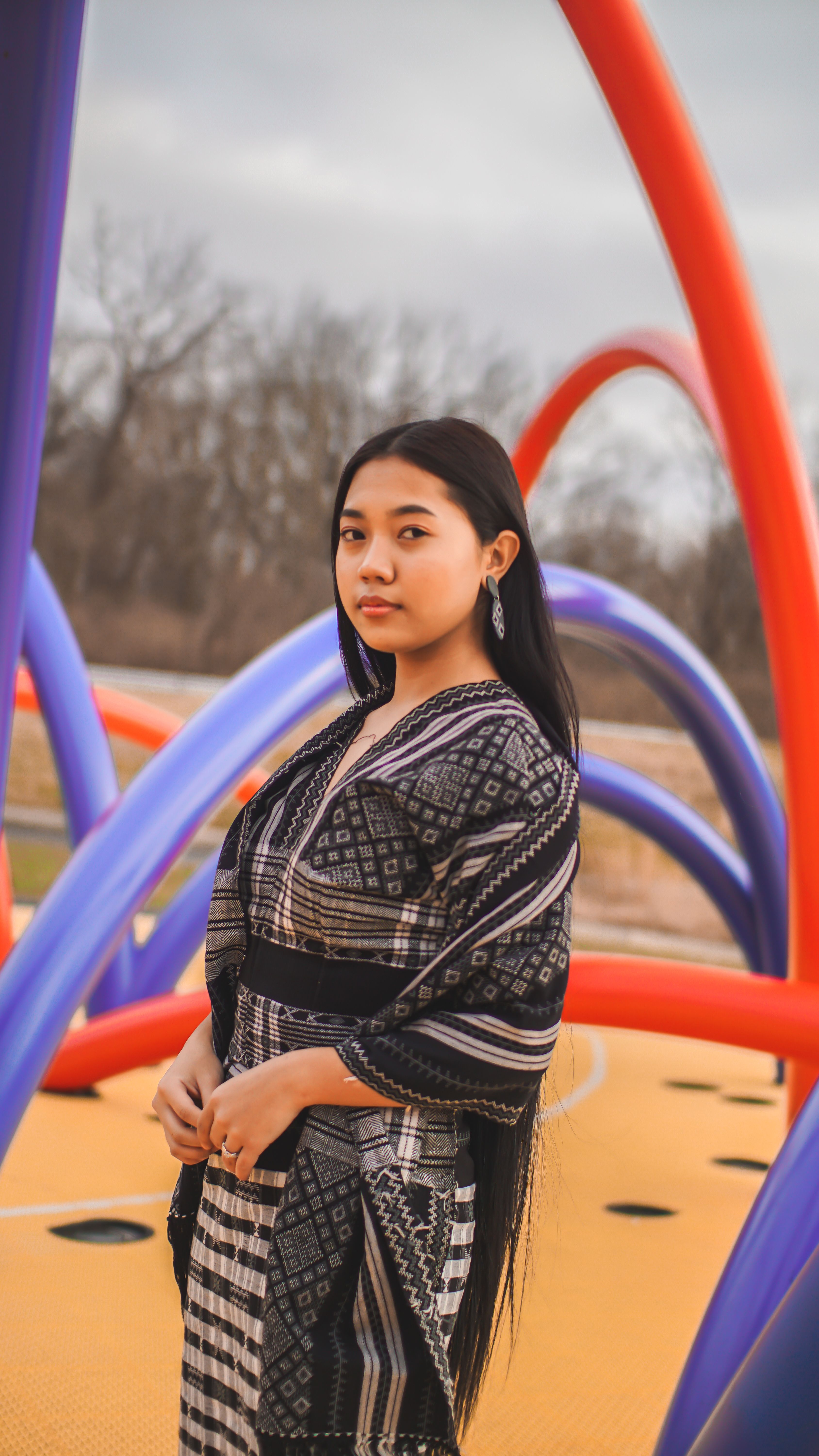 Asian woman wearing traditional clothing stands outdoors among colorful structures