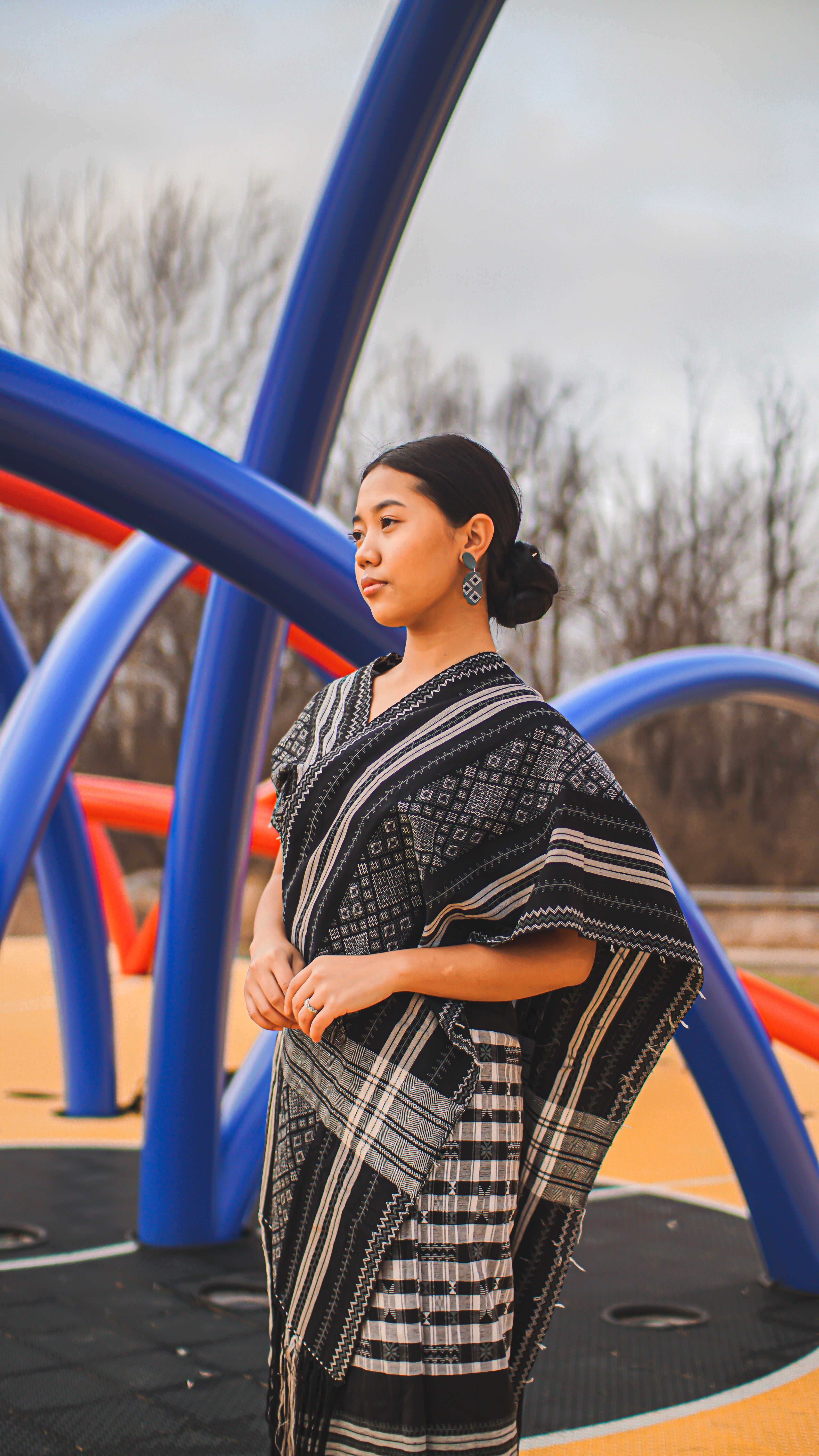 Asian woman in traditional clothing posing outdoors with colorful sculptural backdrop.