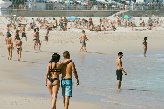 Crowded beach scene with tourists enjoying a sunny day and ocean waves.
