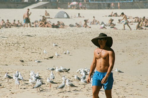 Free Man in Blue Shorts and Brown Hat Walking on Beach Stock Photo