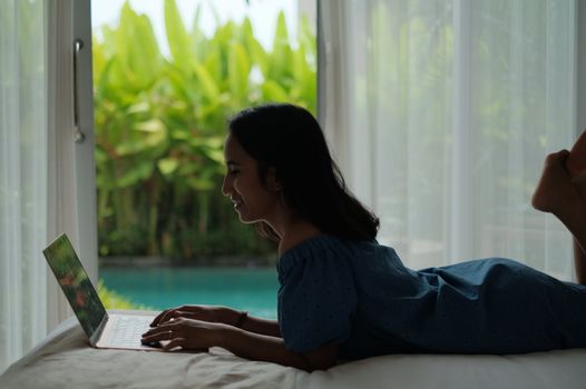 Asian woman working on a laptop indoors in Bali, enjoying a relaxed digital nomad lifestyle.